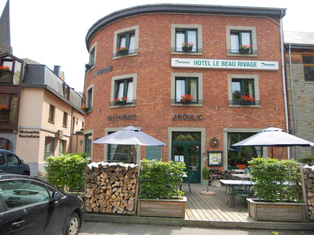 een bakstenen gebouw met tafels en parasols ervoor bij Hotel Beau Rivage and Restaurant Koulic in La-Roche-en-Ardenne