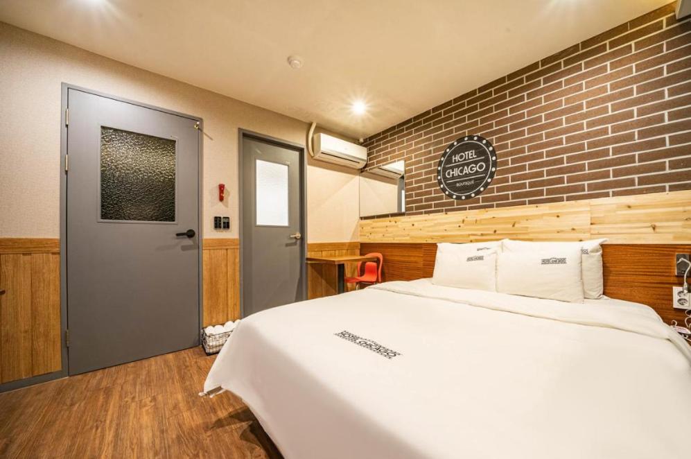 - une chambre avec un lit blanc et un mur en briques dans l'établissement Hotel Chicago, à Jinju