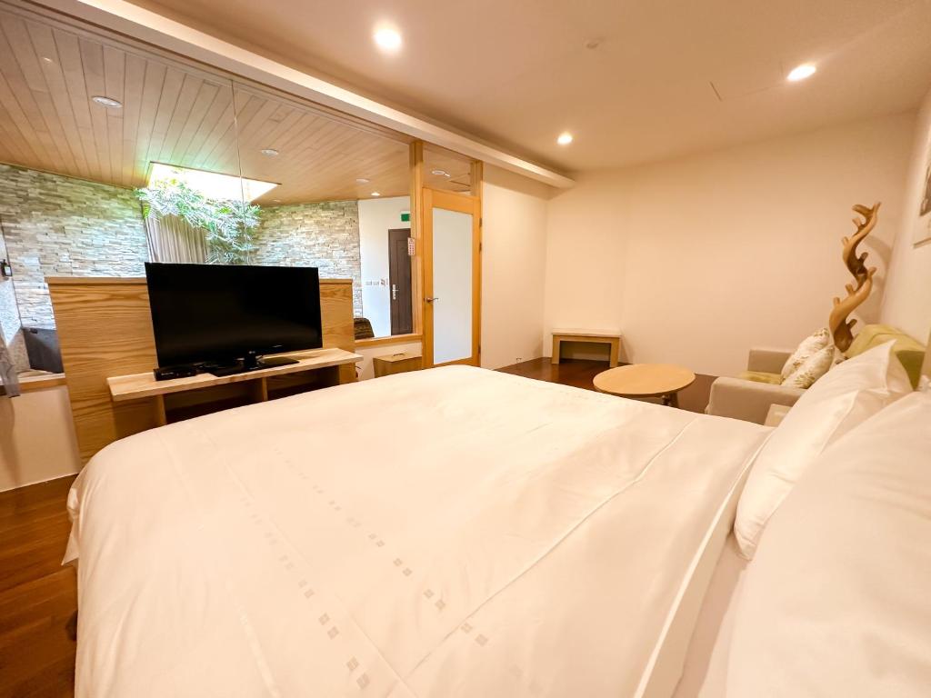 a bedroom with a large white bed and a flat screen tv at Yage Hotspring House in Jiaoxi