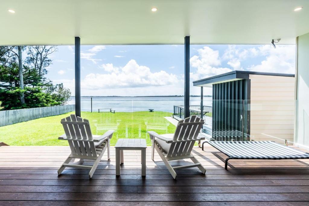 two chairs and a table on a deck with a view of the ocean at On The Corso - Sun-soaked Serenity with Lake Access in Gorokan