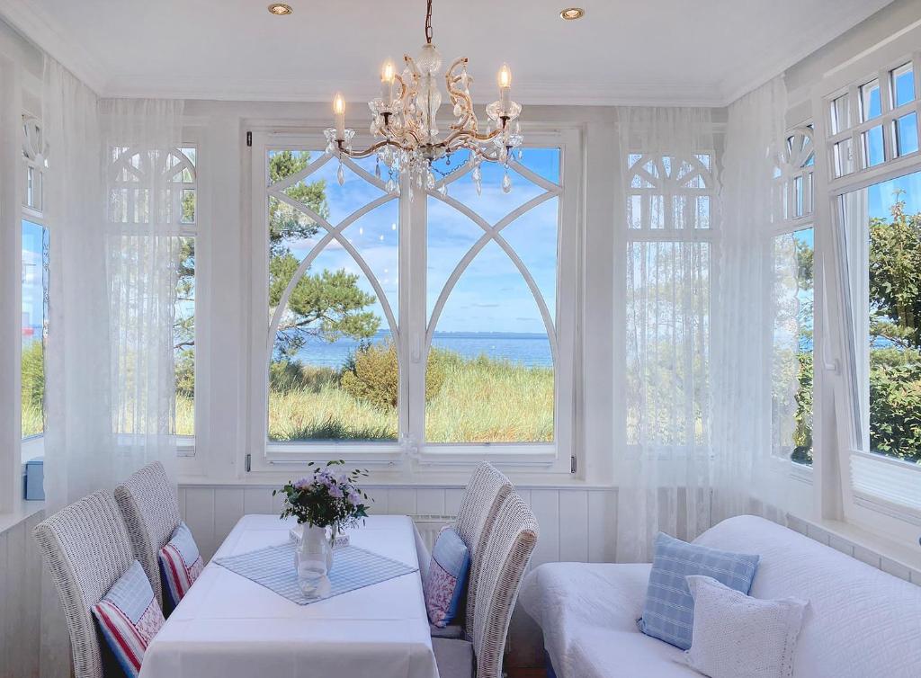 ein Wohnzimmer mit einem Kronleuchter, einem Tisch und Fenstern in der Unterkunft Villa Hansa am Meer in Timmendorfer Strand