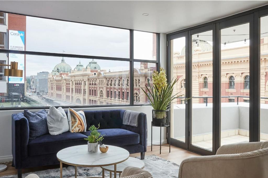 a living room with a blue couch and a large window at Found at Flinders - An Iconic City Stay in Melbourne