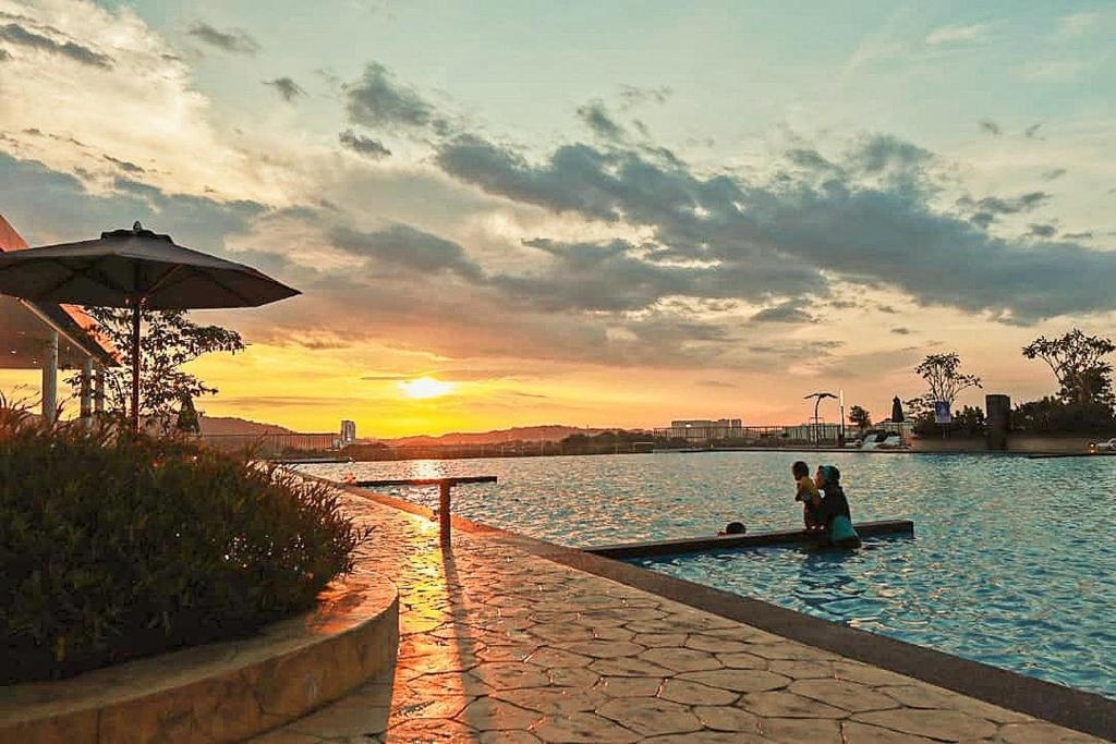 two people sitting in a pool of water at sunset at Palmyra Residence in Kajang