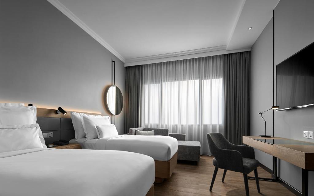 A twin room with two beds, a wall-mounted television, desk and window-side sofa.