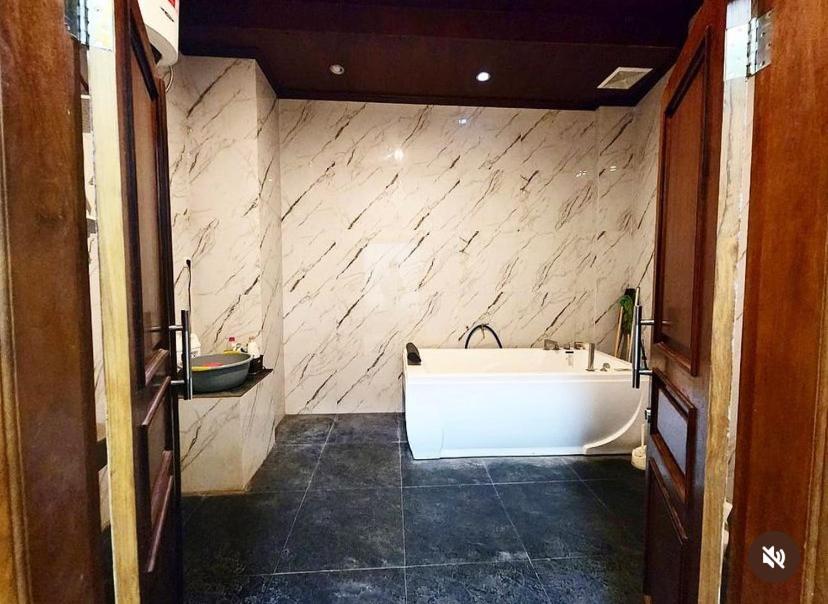 La salle de bains est pourvue d'une baignoire blanche et d'un mur en pierre. dans l'établissement Tumungkul Homestay, à Jejeran