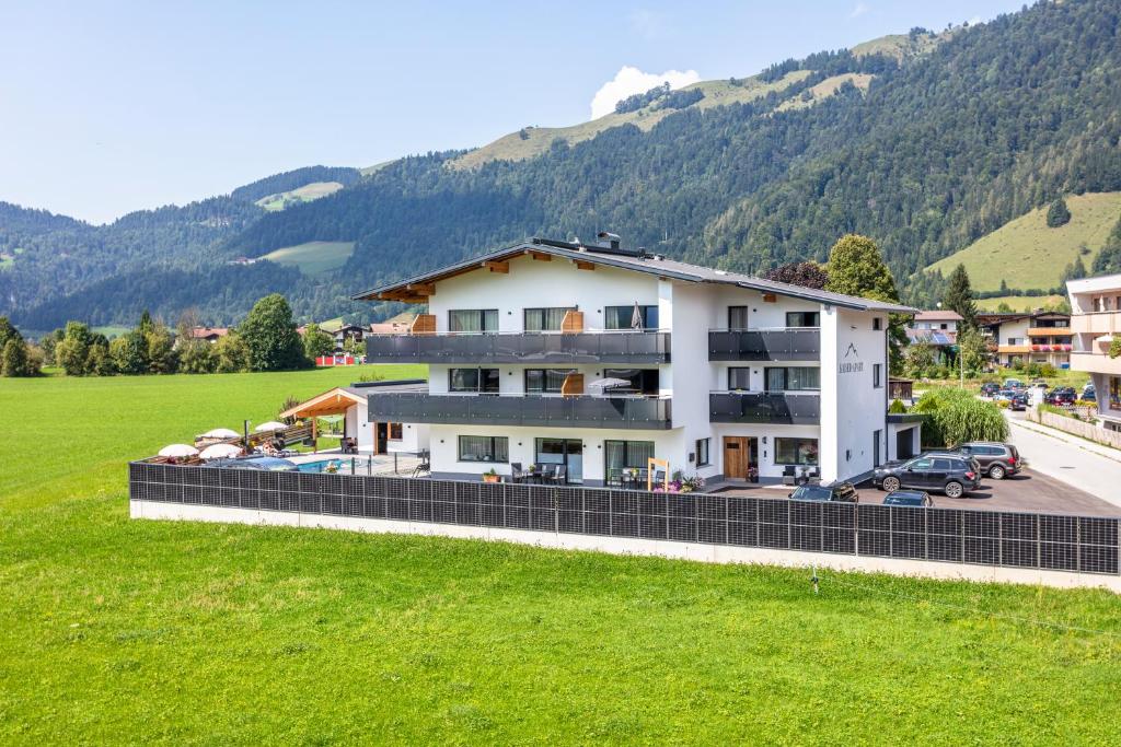a large white building with a green field and mountains at Kaiser Apart Walchsee - Familie Hall in Walchsee