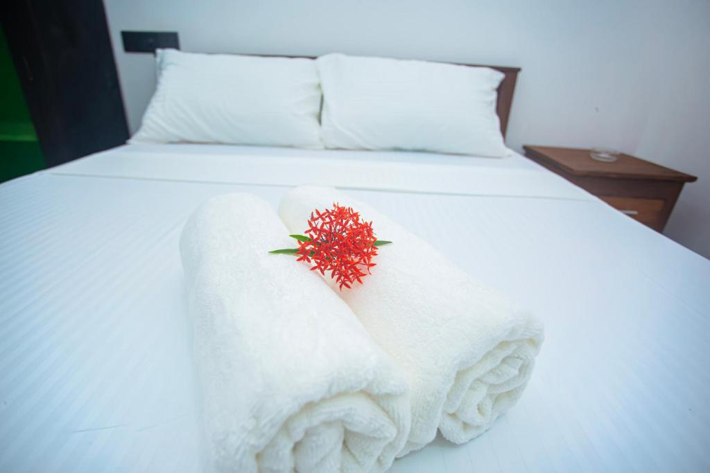 Una cama blanca con toallas blancas y una flor roja. en DR. Place en Hikkaduwa