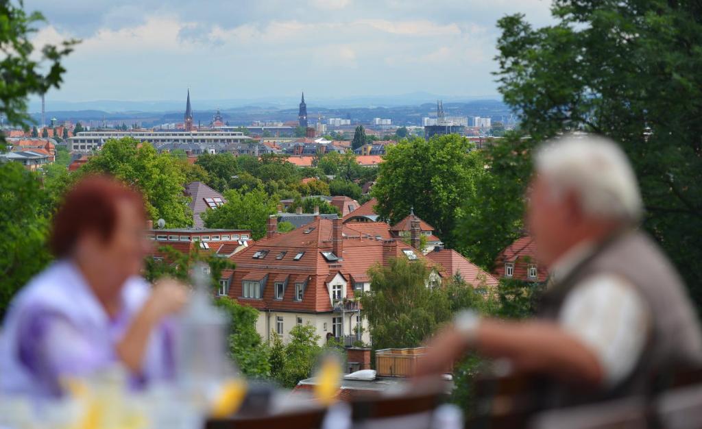 dwoje ludzi siedzących przy stole i patrzących na miasto w obiekcie Bergwirtschaft Wilder Mann Hotel und Restaurant w Dreźnie