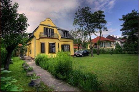 a yellow house with a car parked in a yard at Pálma Apartmanház Siófok in Siófok