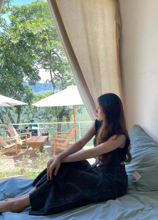 a woman sitting on a bed looking out a window at Retro Khe Sanh in Lao Bao