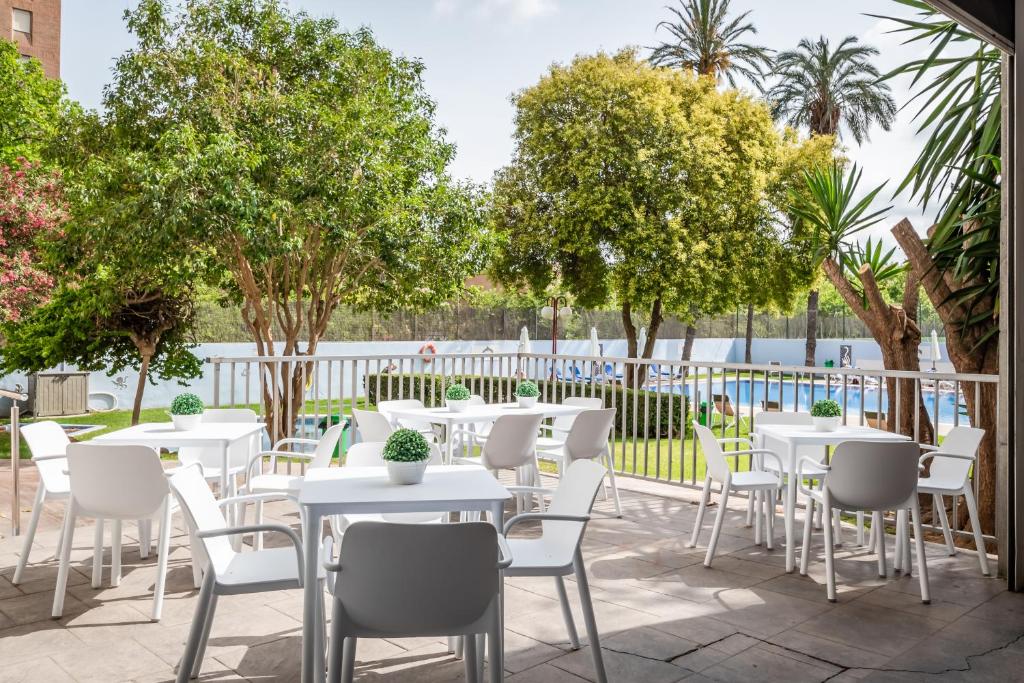 un patio con mesas blancas, sillas y árboles en Hotel Medium Valencia en Valencia