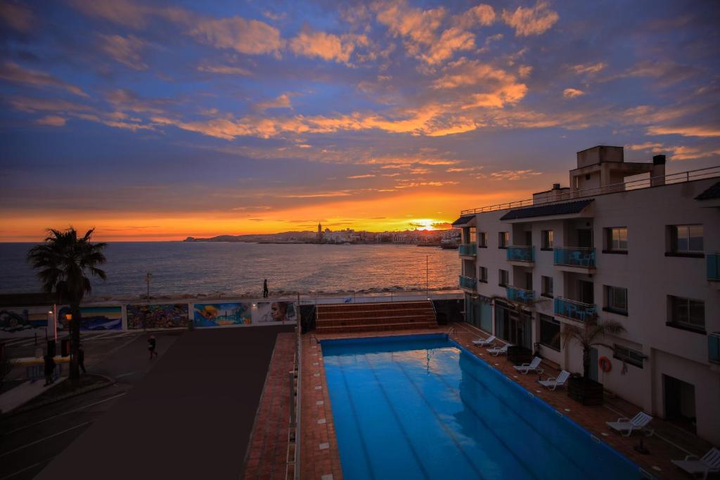 - une vue sur un bâtiment et une piscine au coucher du soleil dans l'établissement Hotel Port Sitges, à Sitges