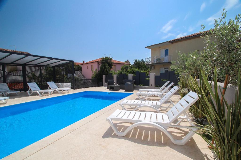 a swimming pool with white lounge chairs next to a house at Apartments Villa Rivarella in Novigrad Istria