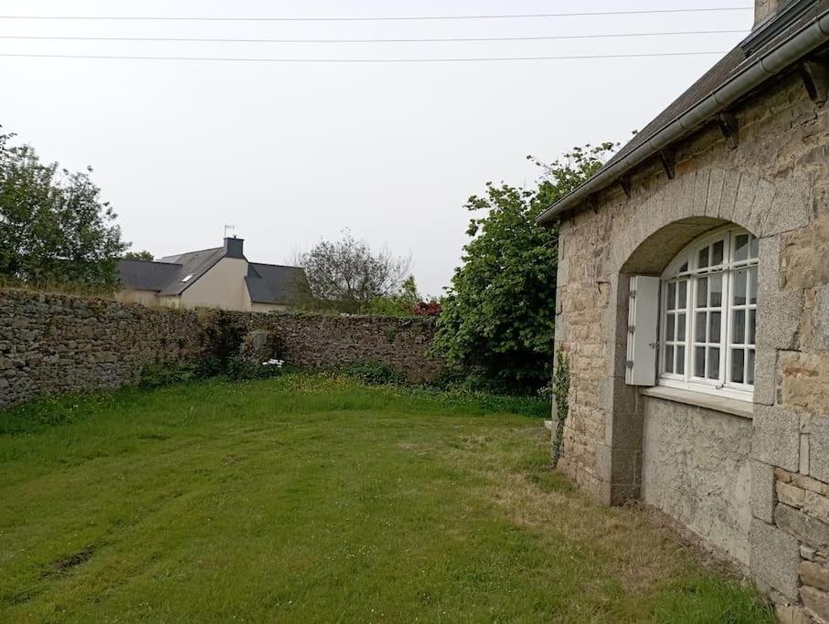 a stone wall with a yard next to a building at Cottage chaleureux à 25 mn de la côte de granit rose in Bégard
