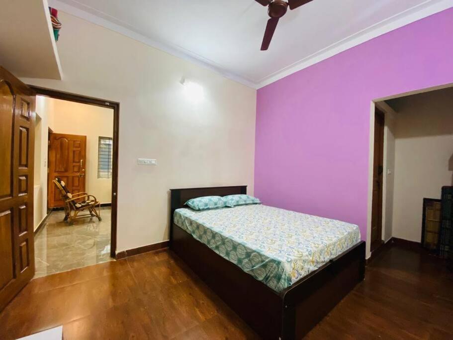 ein Schlafzimmer mit einem Bett und einer lila Wand in der Unterkunft Pal's Cottage in Mysore