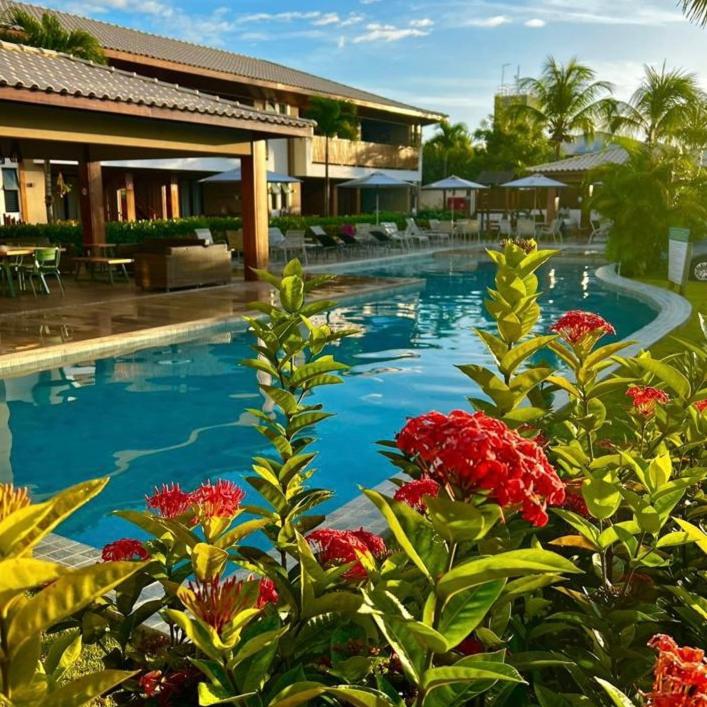 a swimming pool in front of a building with red flowers at Loft de praia - Itacimirim BAHIA in Itacimirim