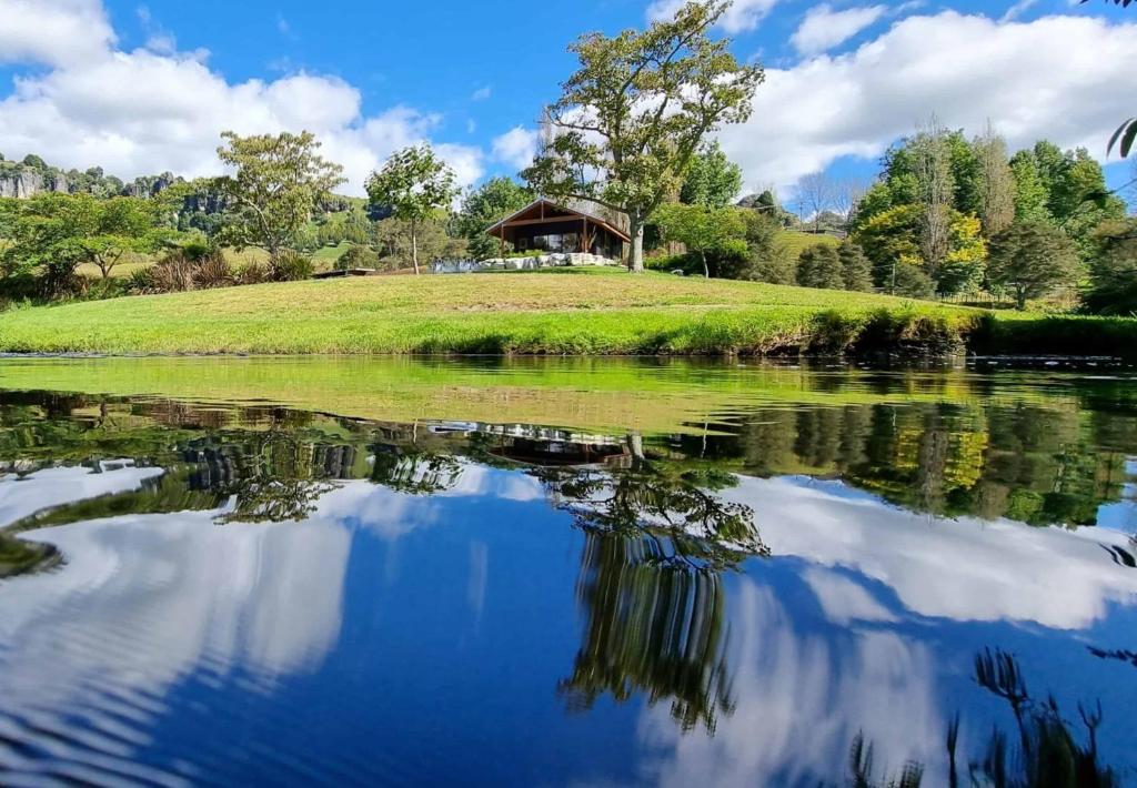 a reflection of a house on a hill in a lake at Ripples Retreat - Riverside in Piopio