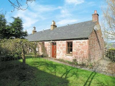 una casa de ladrillo con una puerta roja en un patio verde en Willow Cottage en Kirriemuir