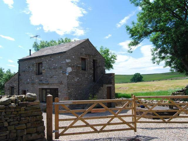 a stone building with a wooden fence in front of it at Skellgill Barn in Bainbridge