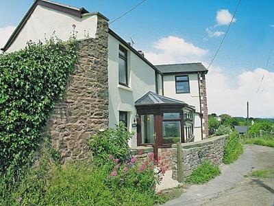 a white house with a stone wall and a fence at Vale View Cottage in Cinderford