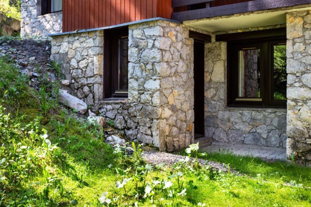 une maison en pierre avec des fenêtres et une colline herbeuse dans l'établissement Résidence Plagne Lauze - maeva Home - Studio 4 Personnes - Sélection MAE-3584, à Mâcot La Plagne