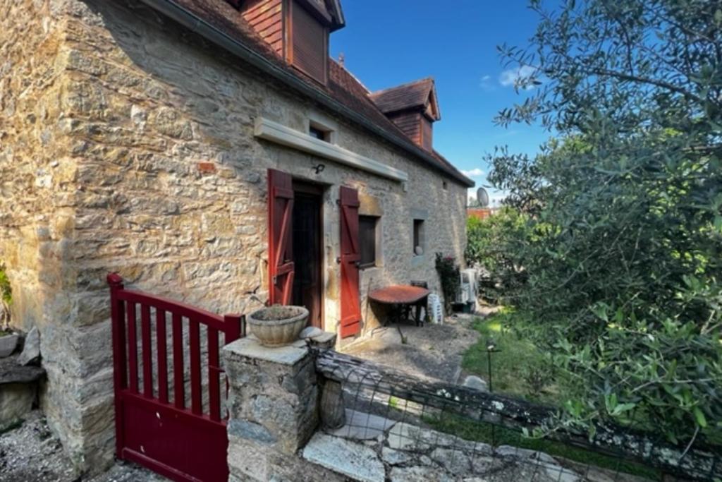 una antigua casa de piedra con una valla roja en L'Oustal de l'Olivier, en Rignac