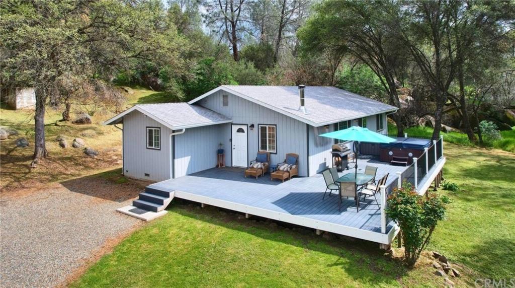 uma pequena casa com um grande deque com uma mesa em Brookside Cottage em Mariposa