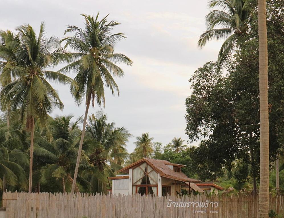 a house behind a fence in front of palm trees at บ้านพราวพร้าว Baan Proud Proud in Khanom