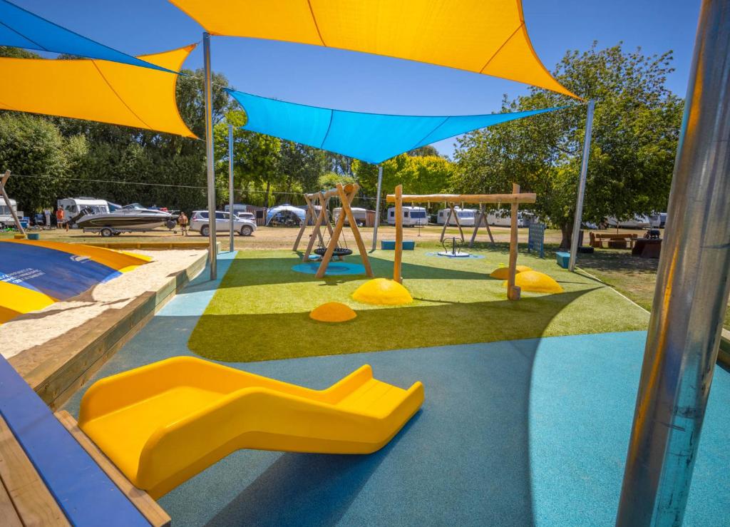 - une aire de jeux avec des toboggans jaunes et un parasol dans l'établissement Omarama TOP10 Holiday Park, à Omarama