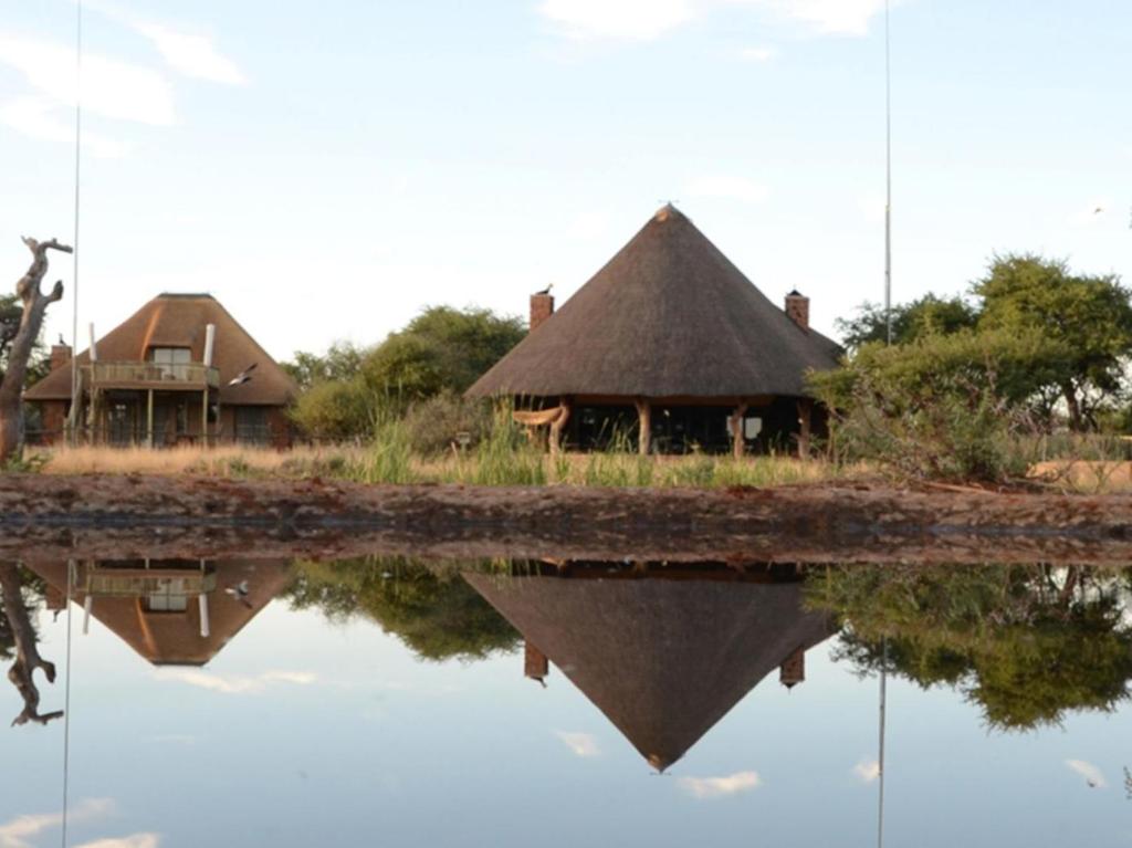 una casa con techo de paja sentada junto a un cuerpo de agua en Mattanu Private Game Reserve, en Barkly West