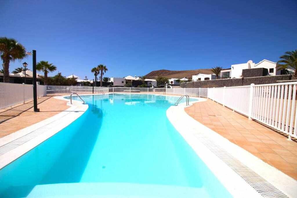een blauw zwembad met een wit hek en palmbomen bij Cotton House in Playa Blanca