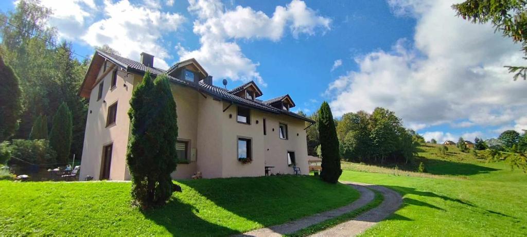 a house on a grassy hill with trees in front of it at Pokoje u Juroszka in Istebna