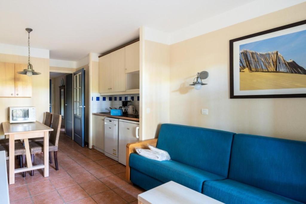 un salon avec un canapé bleu et une cuisine dans l'établissement Résidence Lacanau Les Pins - maeva Home - Appartement 2 Pièces 4 Personnes - Sélection MAE-7335, à Lacanau