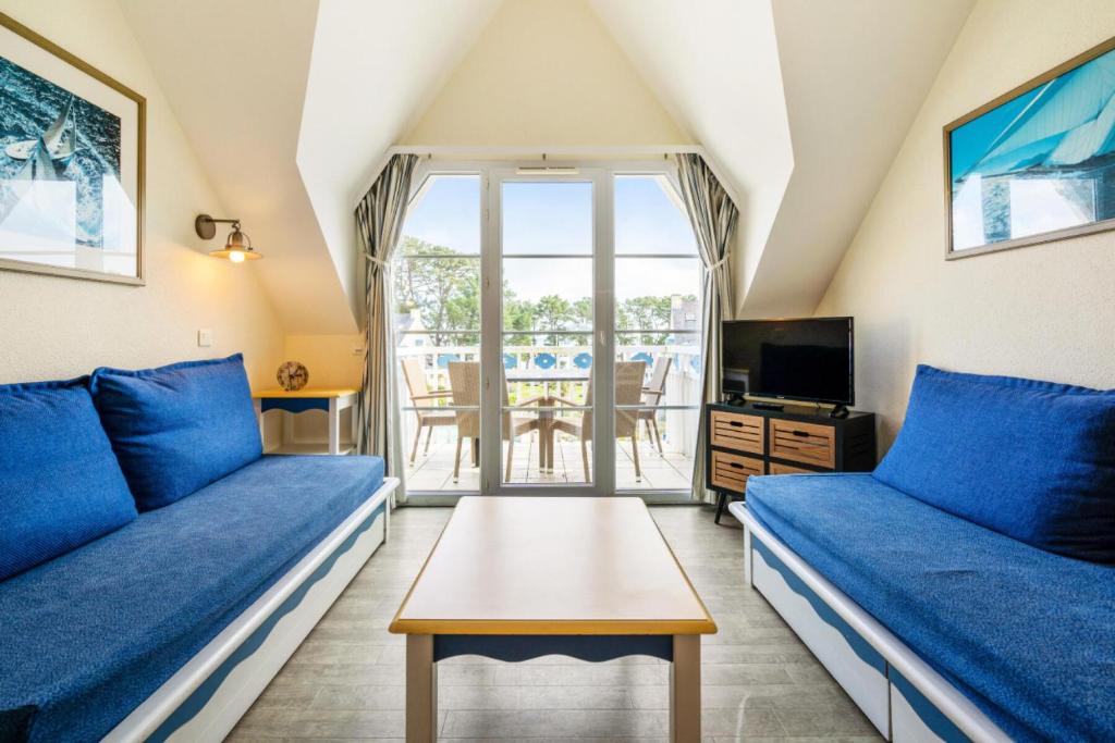 un salon avec des canapés bleus et une télévision dans l'établissement Résidence Cap Azur - maeva Home - Appartement duplex 2 Pièces 5 Personnes Sélection - Vue mer MAE-1182, à Fouesnant