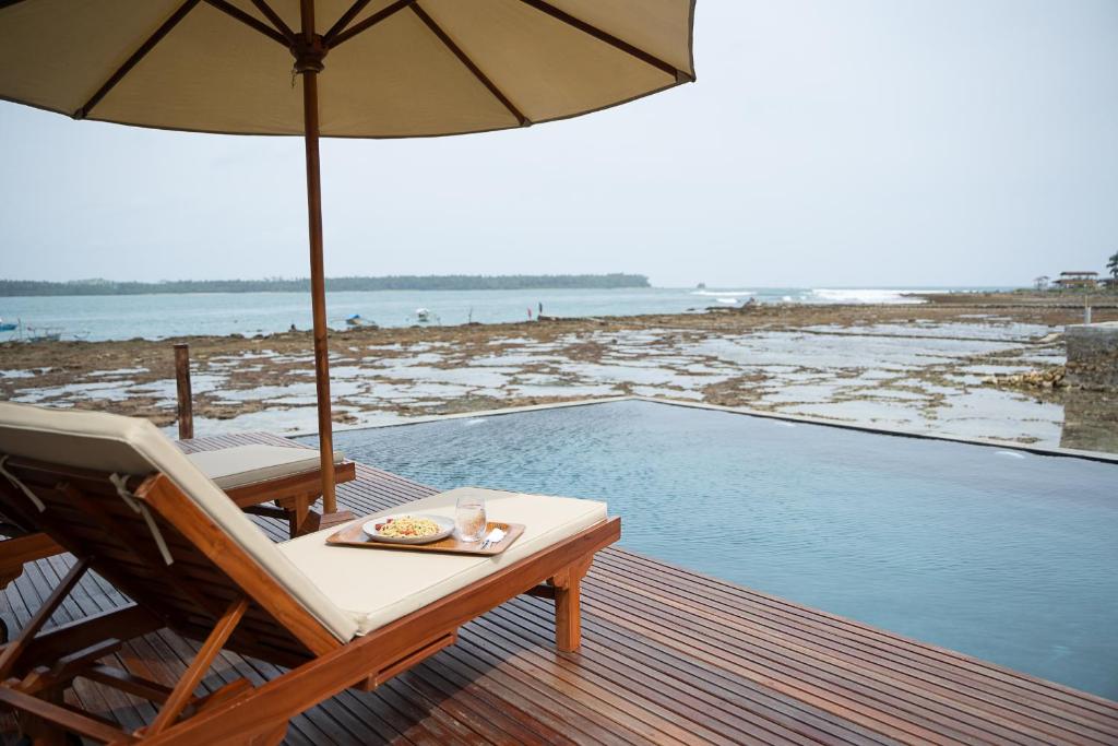 une chaise et un parasol sur une terrasse à côté de la piscine dans l'établissement HIMA Bungalows, à Lagudri