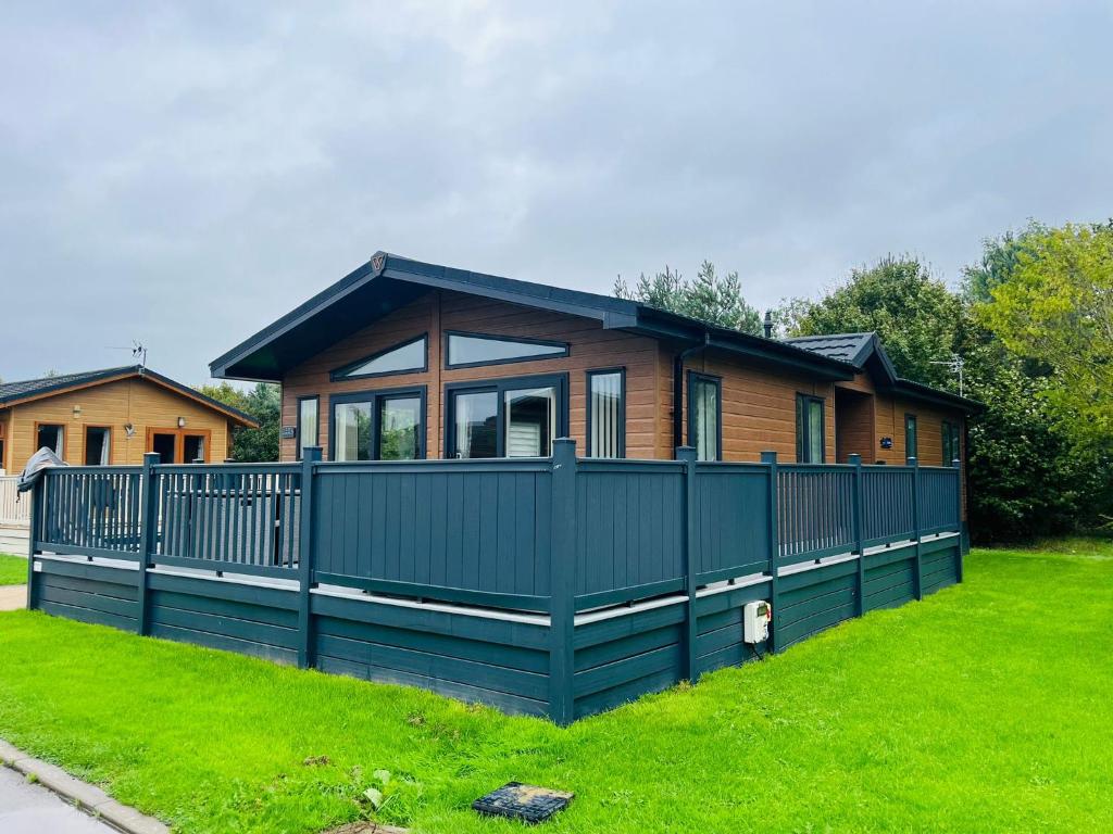 a house with a green fence in the grass at Blue Bell Lodge with Hot Tub Malton in Little Habton