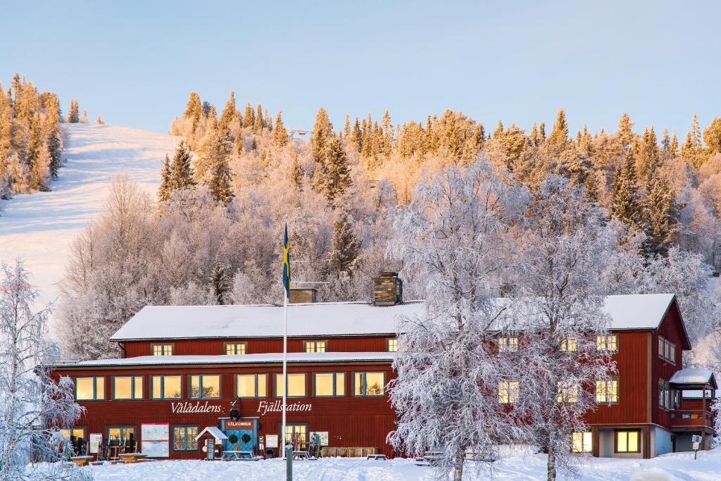 um grande edifício vermelho na neve com árvores em Vålådalens Fjällstation em Vålådalen