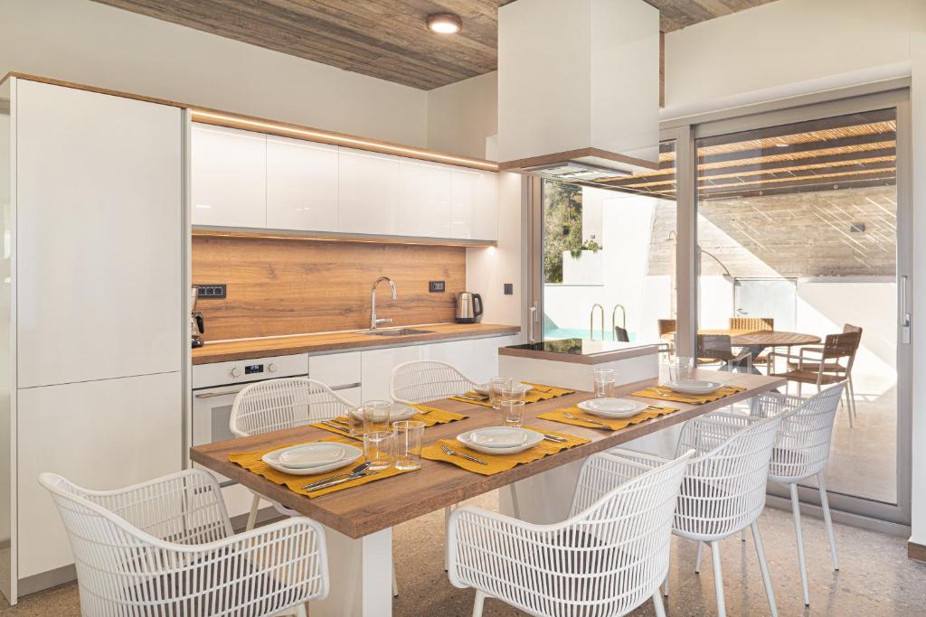 a kitchen with a wooden table and white chairs at New Modern Villa Domus Myrtia with private pool & BBQ, 4km from nearest beach in Marioú