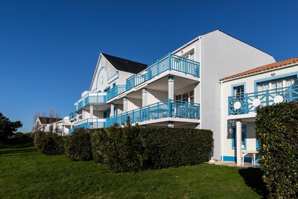 une maison blanche avec des balcons bleus sur une pelouse dans l'établissement Résidence Port Bourgenay - maeva Home - Appartement 2 pièces 7 personnes - Confort MAE-7054, à Talmont-Saint-Hilaire