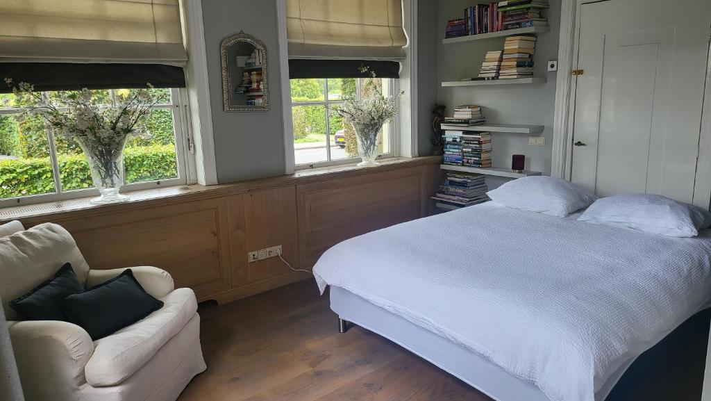 a bedroom with a bed and a chair and windows at Amsterdam Mansion - The Studio in Oostzaan