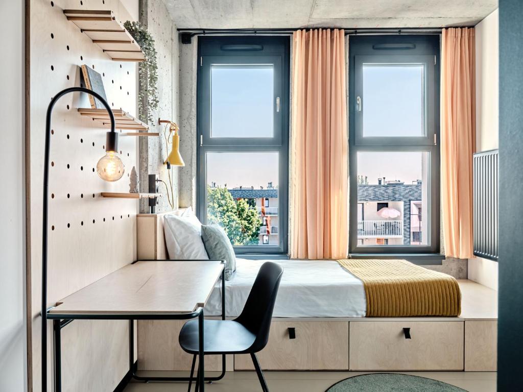 a bedroom with a bed and a desk and windows at Basecamp Wroclaw in Wrocław