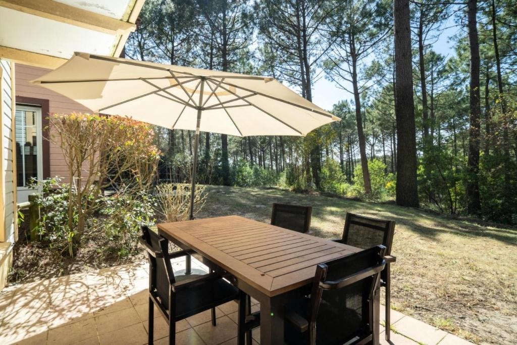 une table et des chaises en bois avec un parasol dans l'établissement Les Maisons de Lacanau les Pins - maeva Home - Maison 3 pièces 8 personnes - Sélection MAE-7343, à Lacanau
