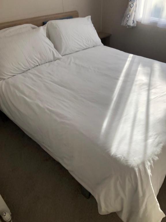Elle comprend un grand lit blanc avec des draps et des oreillers blancs. dans l'établissement Beach house fun, à Walton-on-the-Naze