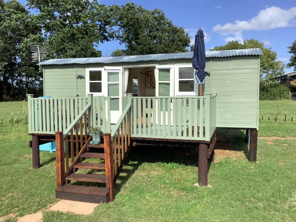 a green tiny house with a porch and an umbrella at Muffins Meadow Shepherds Hut in Tillingham