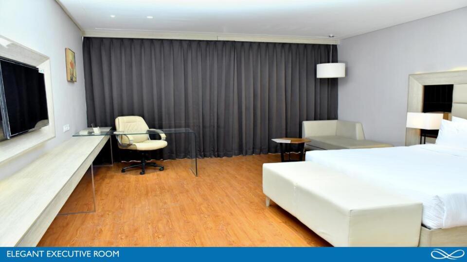 a hotel room with a bed and a desk and a table at Sarovar Portico Morbi in Morbi