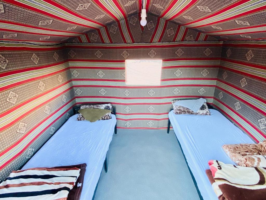 two beds in a small room with striped walls at Wadi Rum Jordan Camp in Wadi Rum
