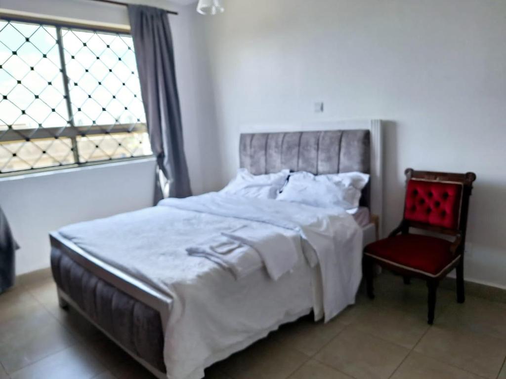 een slaapkamer met een bed en een rode stoel bij Jkia 3 bedroom greatwall gardens phase 4 in Athi River