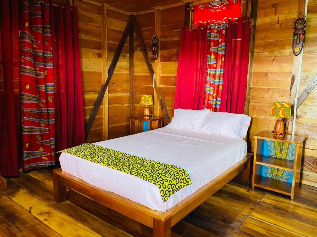 a bed in a room with wooden walls and red curtains at Monte Mar SãoTomé in M. Peixe