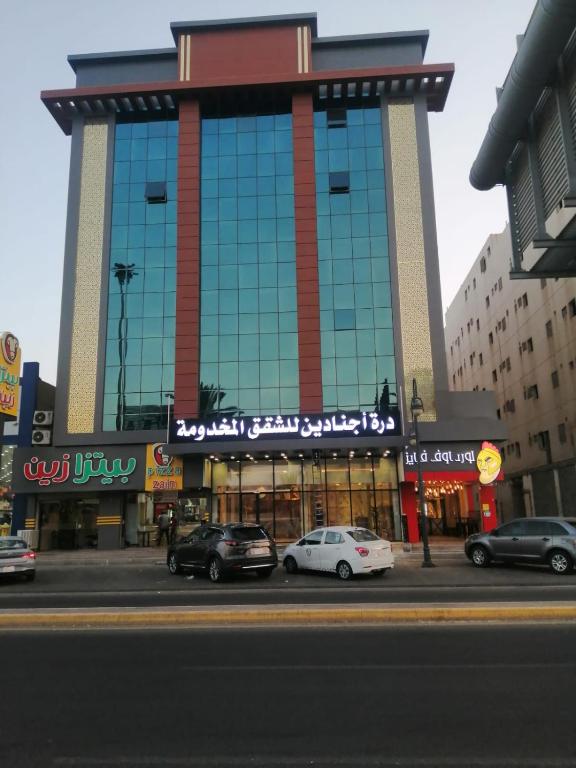 um grande edifício com carros estacionados em frente em درة اجنادين للشقق المخدومة em Tabuk