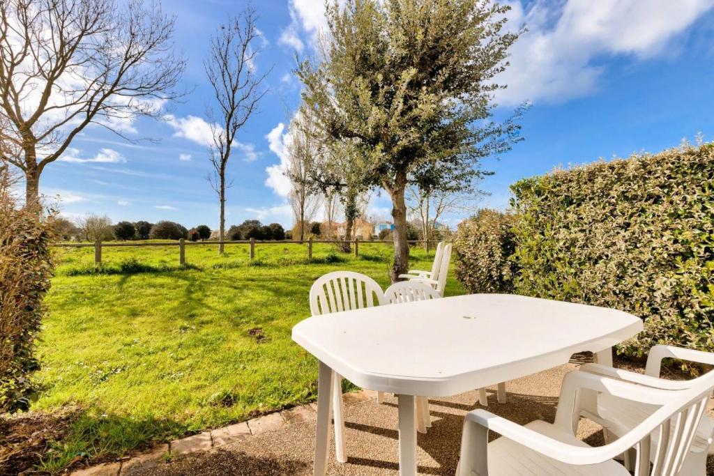 une table et des chaises blanches avec vue sur un champ dans l'établissement Les Maisons de Port Bourgenay - maeva Home - Maison 3 Pièces 6 personnes Confort MAE-0320, à Talmont-Saint-Hilaire